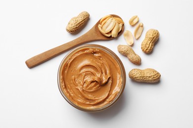 Photo of Tasty peanut butter in bowl and spoon with groundnuts on white table, flat lay