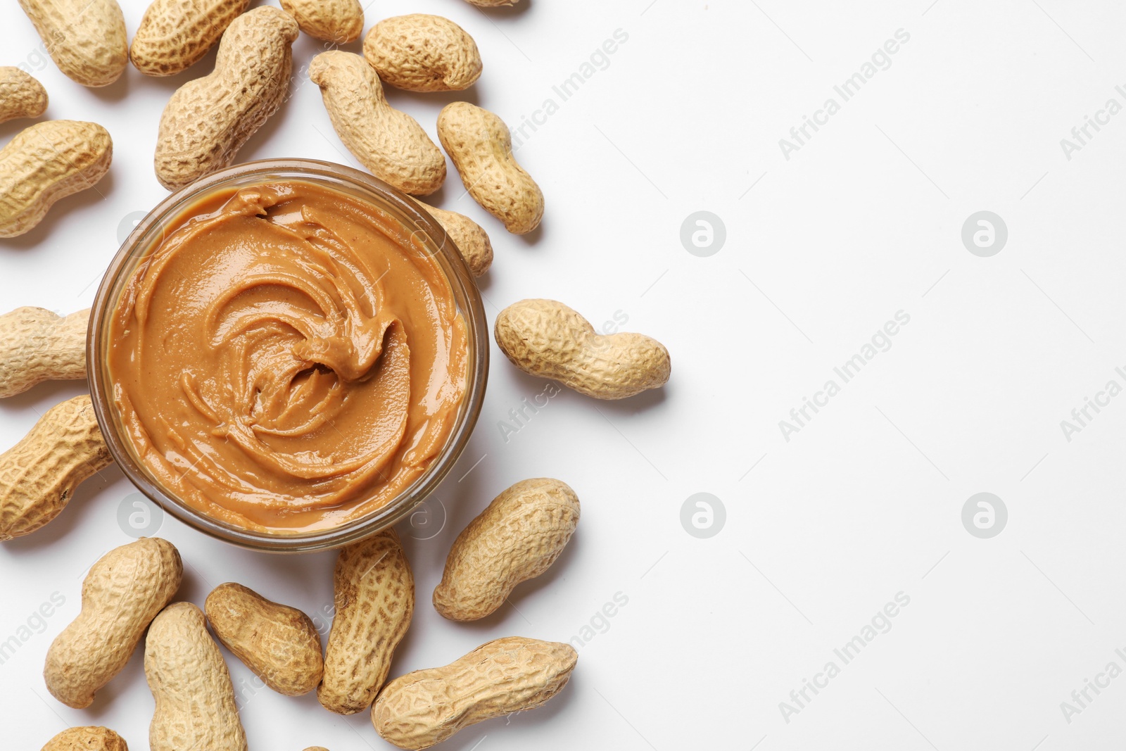 Photo of Tasty peanut butter in bowl and groundnuts on white table, flat lay. Space for text