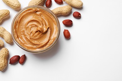 Photo of Tasty peanut butter in bowl and groundnuts on white table, flat lay. Space for text