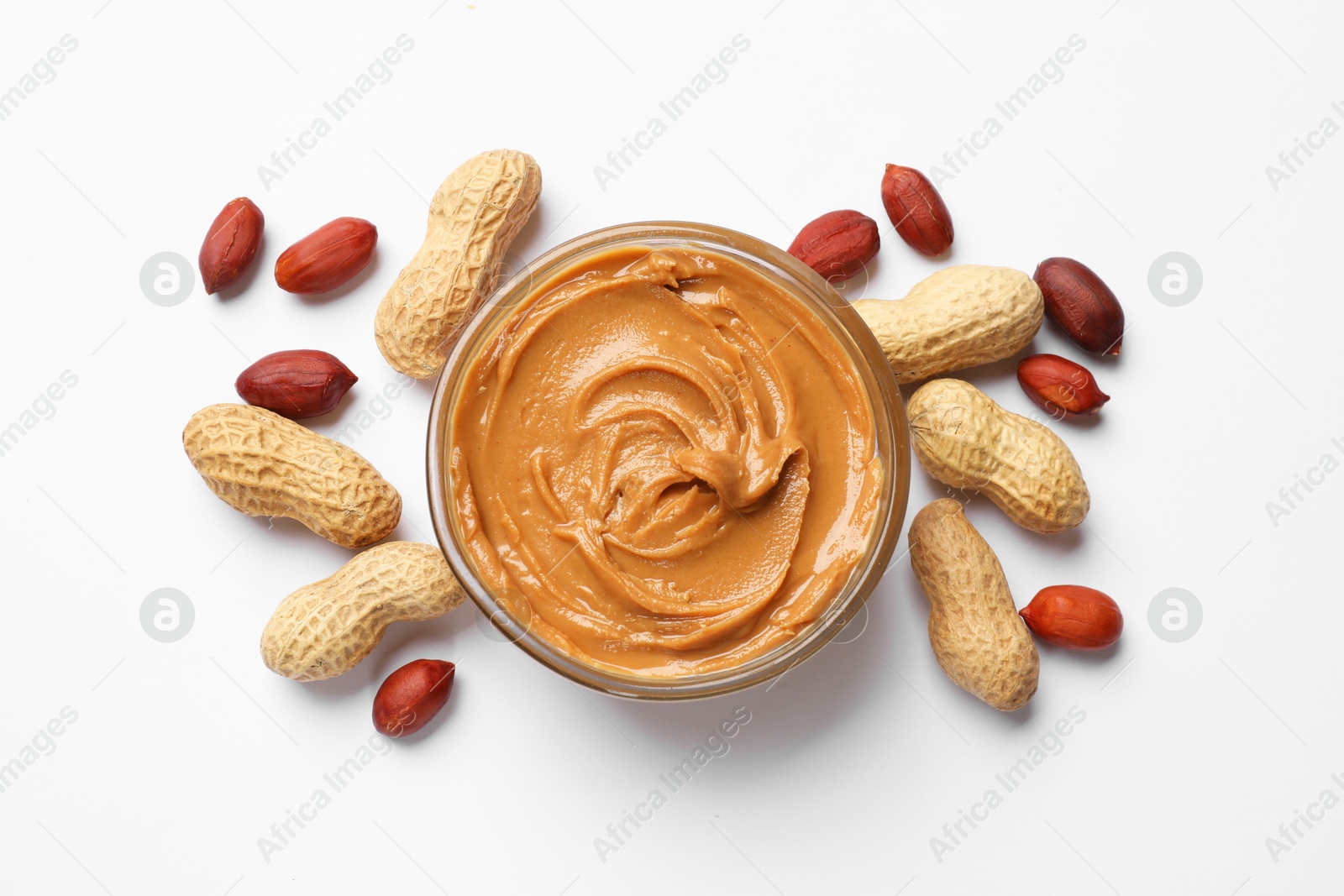 Photo of Tasty peanut butter in bowl and groundnuts on white table, flat lay