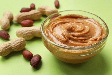 Tasty peanut butter in bowl and groundnuts on green table, closeup