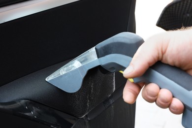 Photo of Man cleaning car door with vacuum cleaner outdoors, closeup