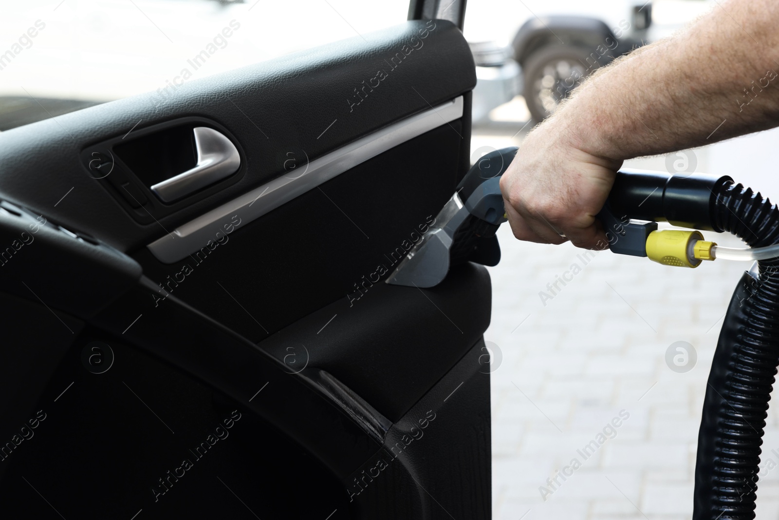 Photo of Man cleaning car door with vacuum cleaner outdoors, closeup