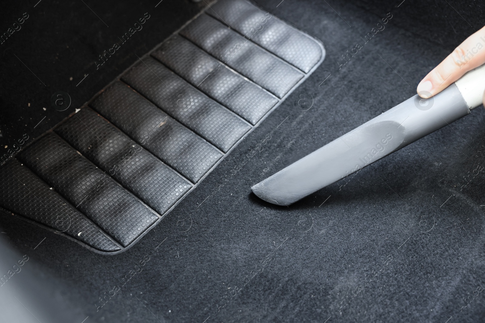 Photo of Man cleaning car floor mat with vacuum cleaner, closeup