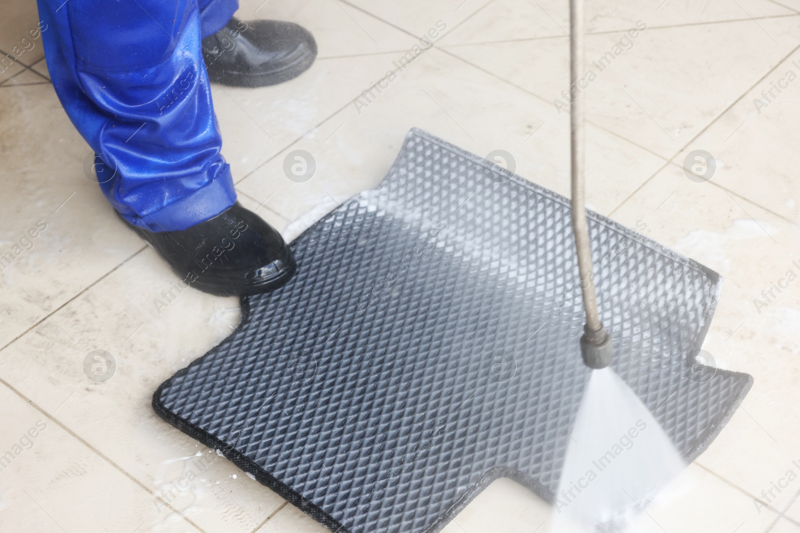 Photo of Man washing rubber car mat with high pressure water jet indoors, closeup