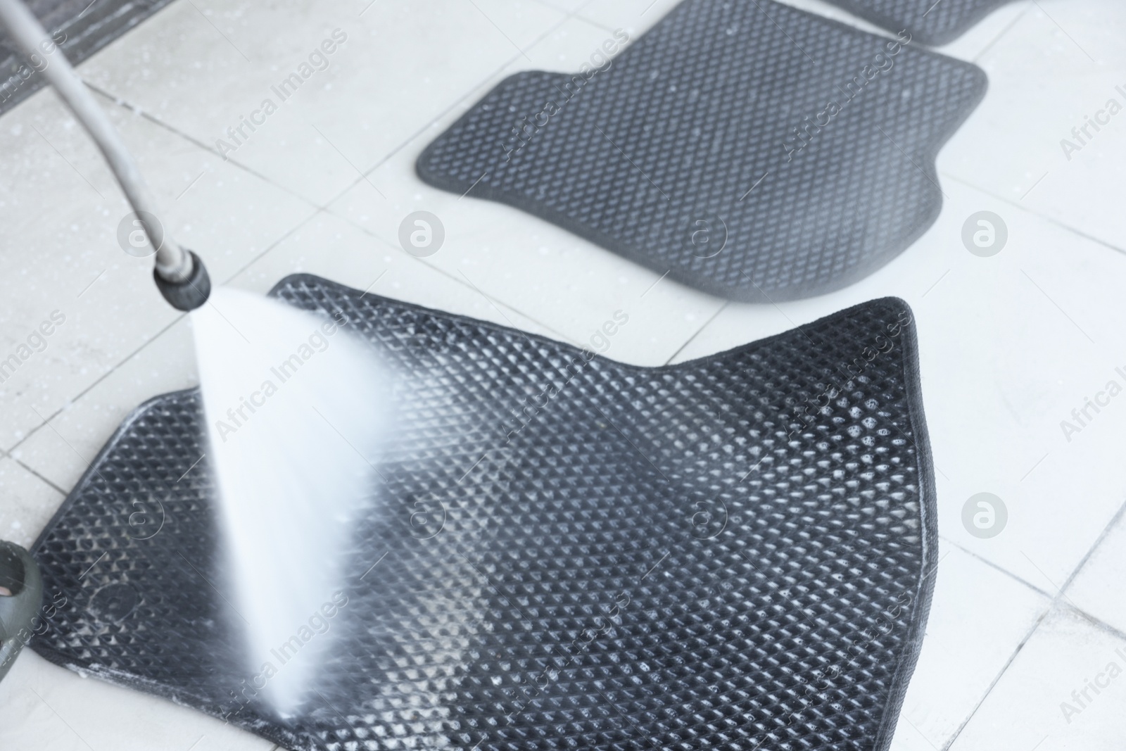 Photo of Washing rubber car mat with high pressure water jet indoors, closeup