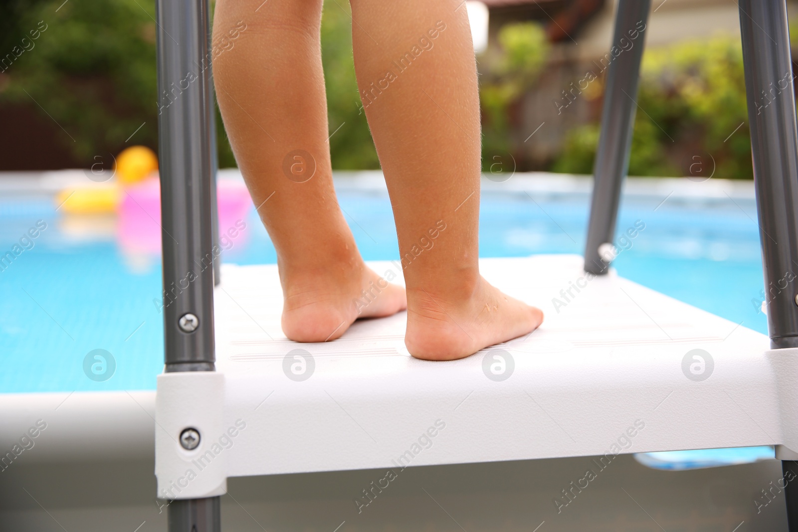 Photo of Little girl on swimming pool ladder outdoors, closeup