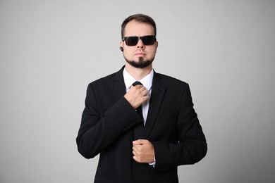 Young bodyguard in suit and sunglasses on grey background