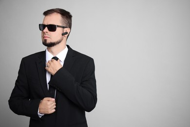 Young bodyguard in suit and sunglasses on grey background, space for text