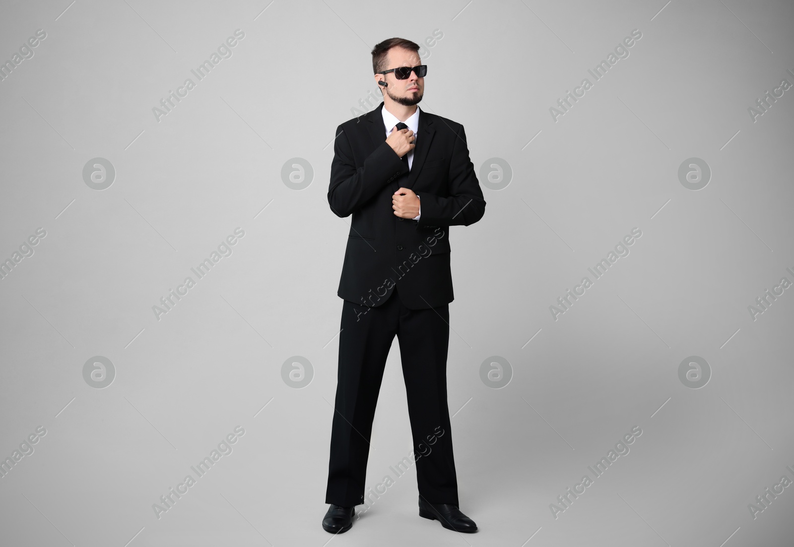 Photo of Young bodyguard in suit and sunglasses on grey background