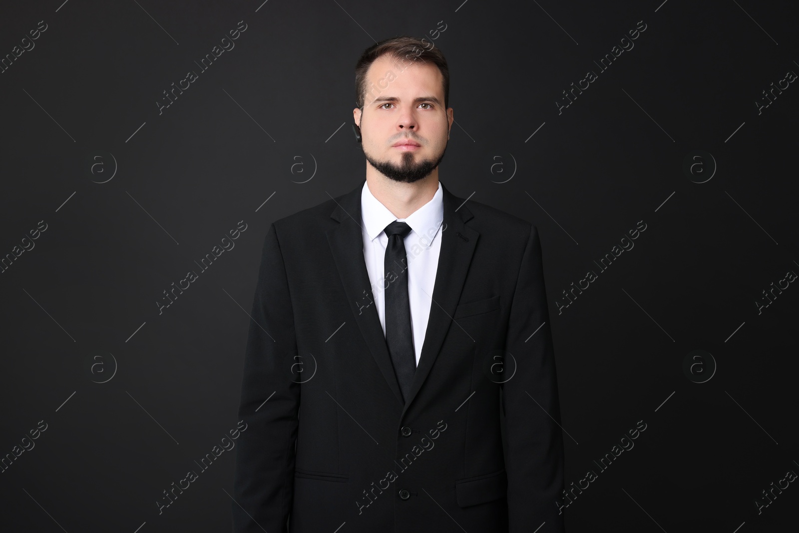 Photo of Young bodyguard in suit with earpiece on black background