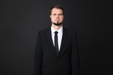 Young bodyguard in suit with earpiece on black background