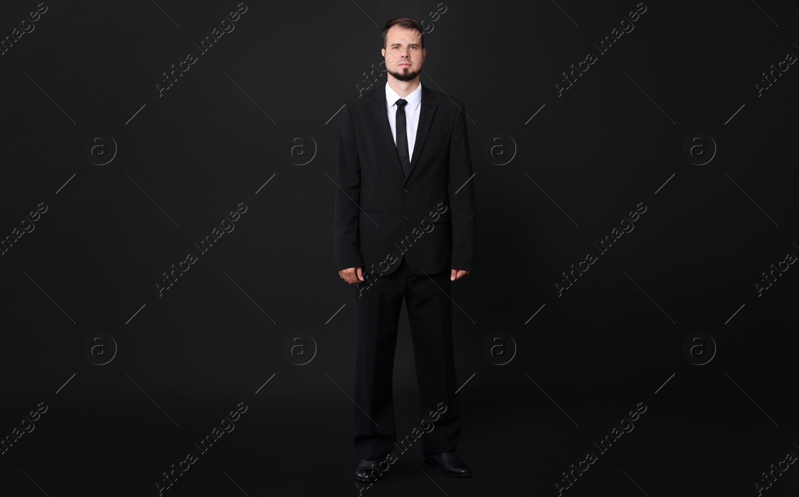 Photo of Young bodyguard in suit with earpiece on black background