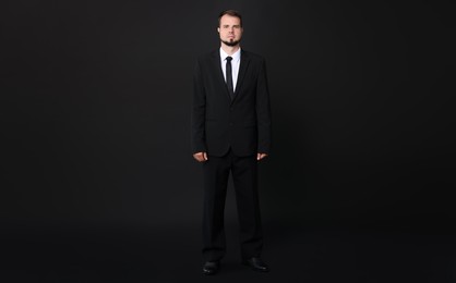 Young bodyguard in suit with earpiece on black background