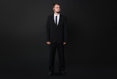 Young bodyguard in suit with earpiece on black background