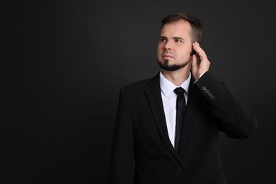 Photo of Young bodyguard in suit with earpiece on black background, space for text