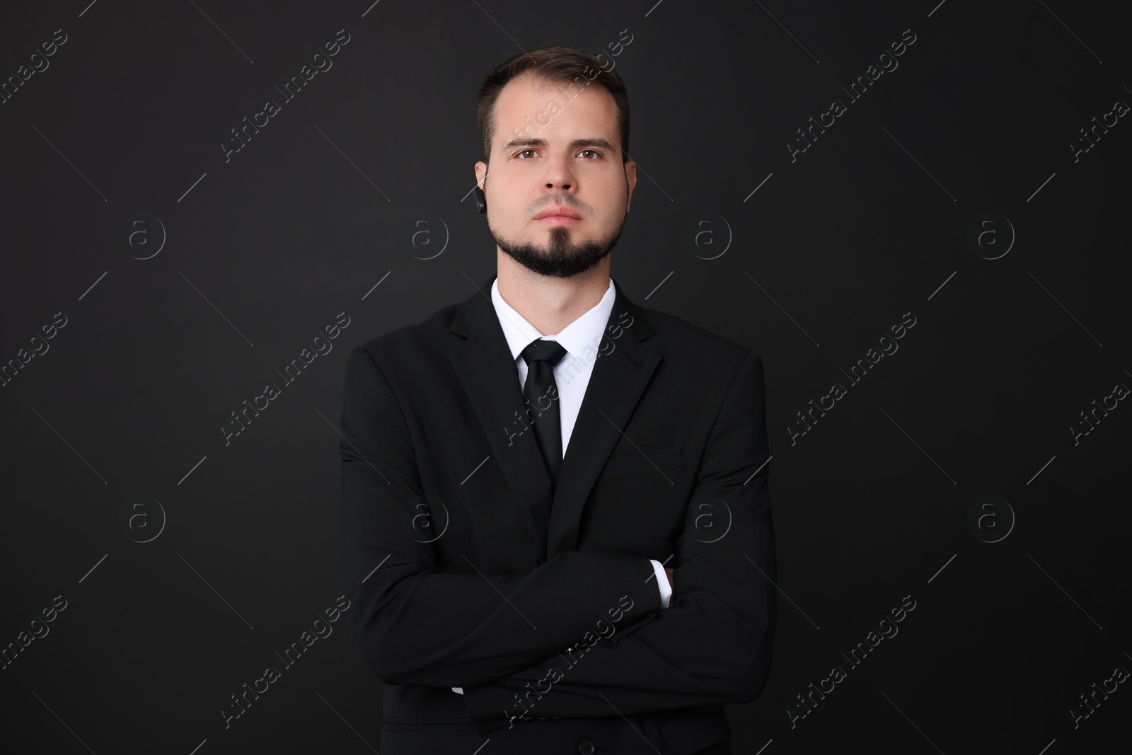 Photo of Young bodyguard in suit with earpiece on black background