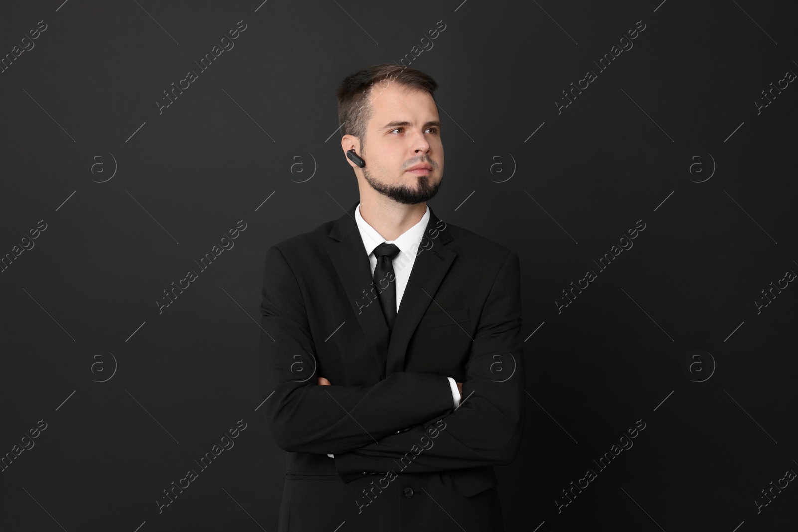 Photo of Young bodyguard in suit with earpiece on black background