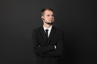 Young bodyguard in suit with earpiece on black background