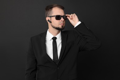 Photo of Young bodyguard in suit with sunglasses on black background