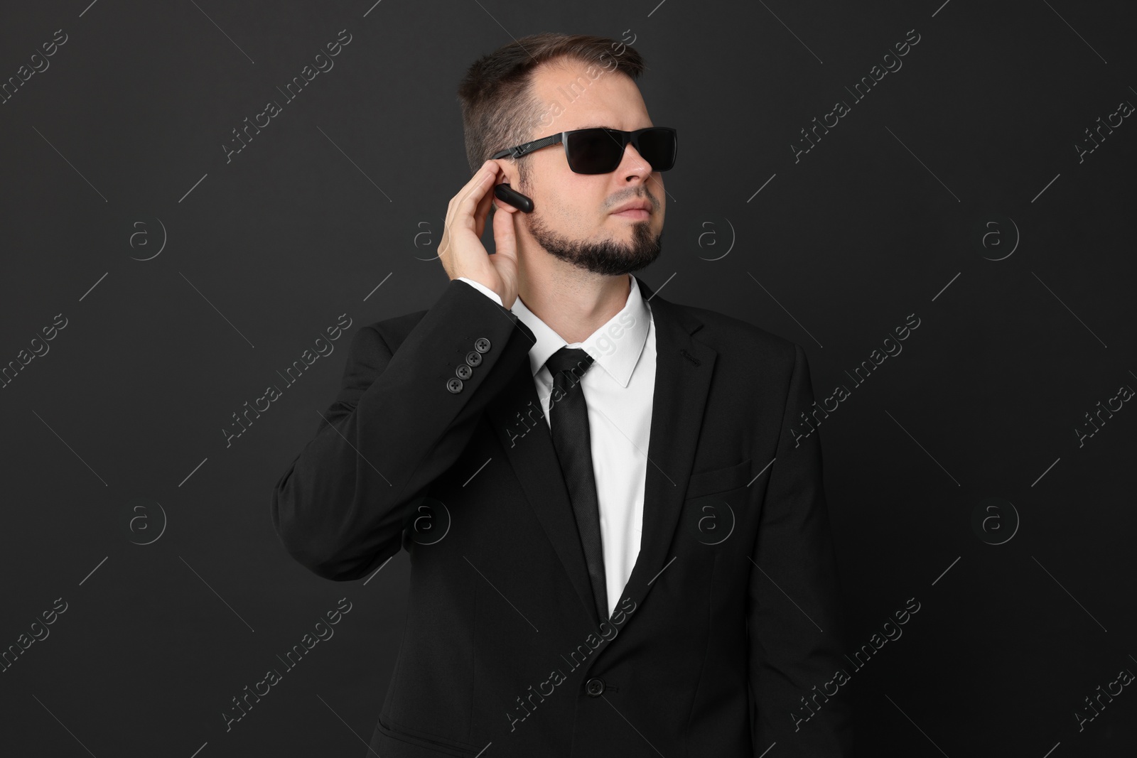 Photo of Young bodyguard in suit with sunglasses on black background