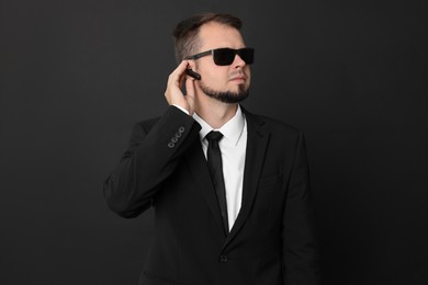 Young bodyguard in suit with sunglasses on black background