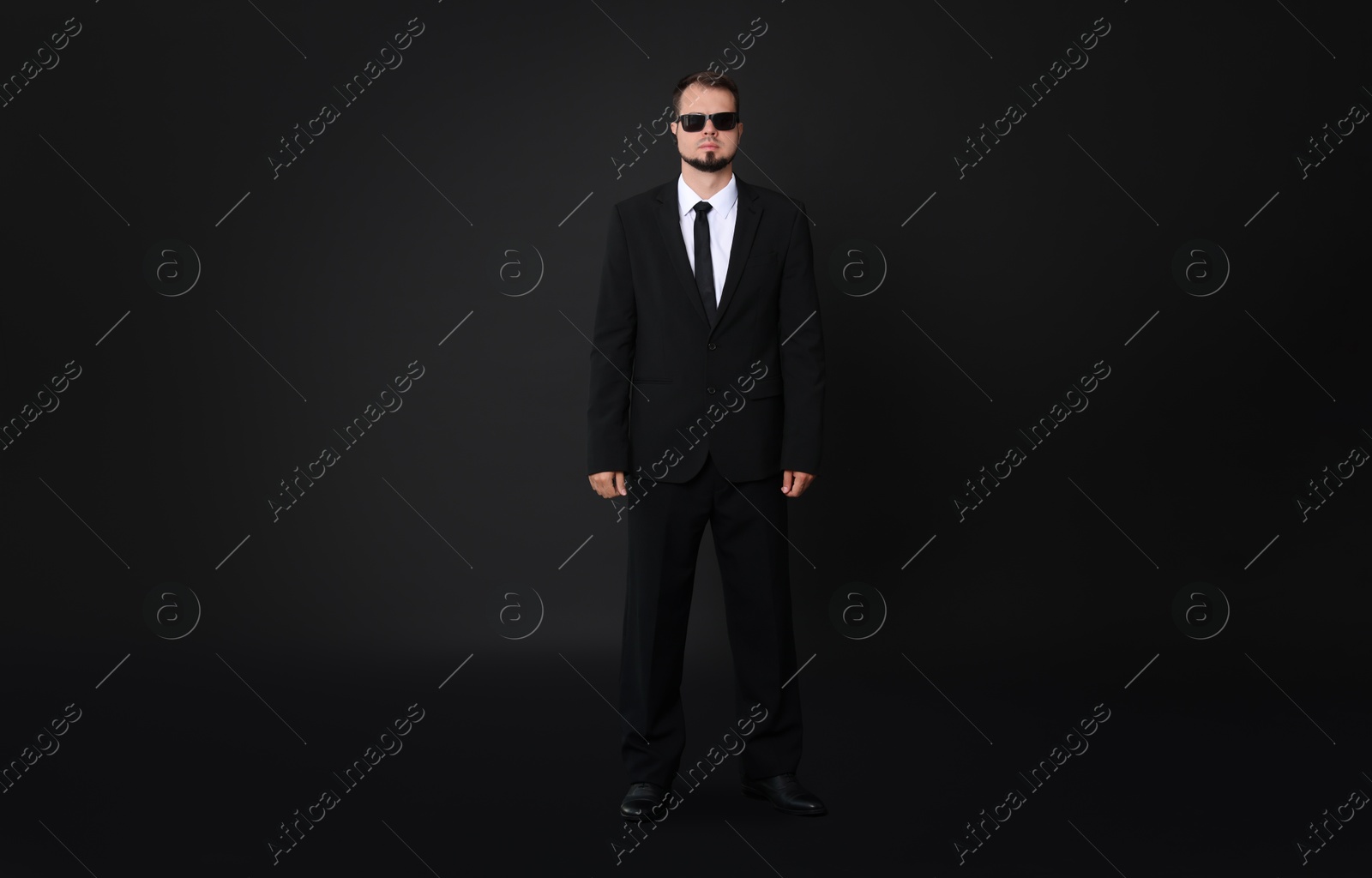 Photo of Young bodyguard in suit with sunglasses on black background