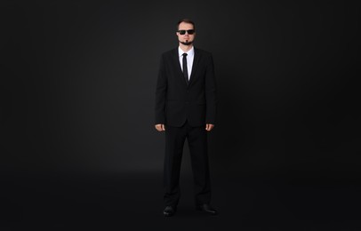 Young bodyguard in suit with sunglasses on black background