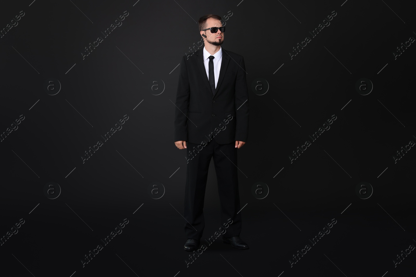 Photo of Young bodyguard in suit with sunglasses on black background