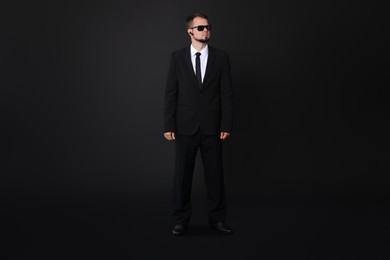 Young bodyguard in suit with sunglasses on black background