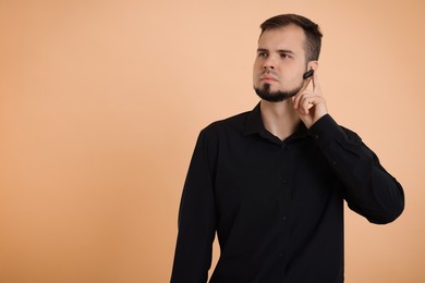 Young bodyguard with earpiece on beige background, space for text