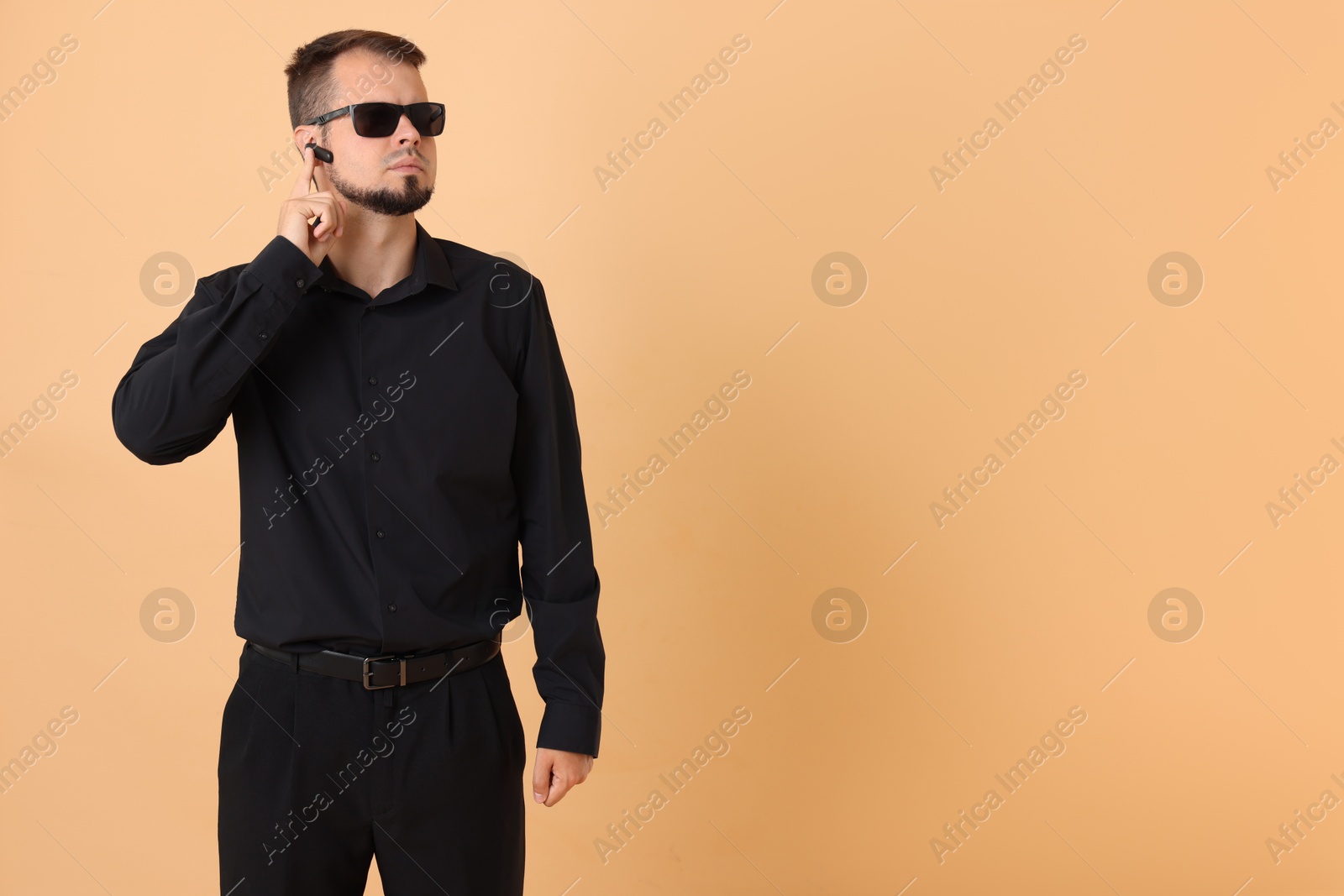 Photo of Young bodyguard in sunglasses and earpiece on beige background, space for text