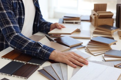 Photo of Man choosing wooden flooring among different samples at table, closeup