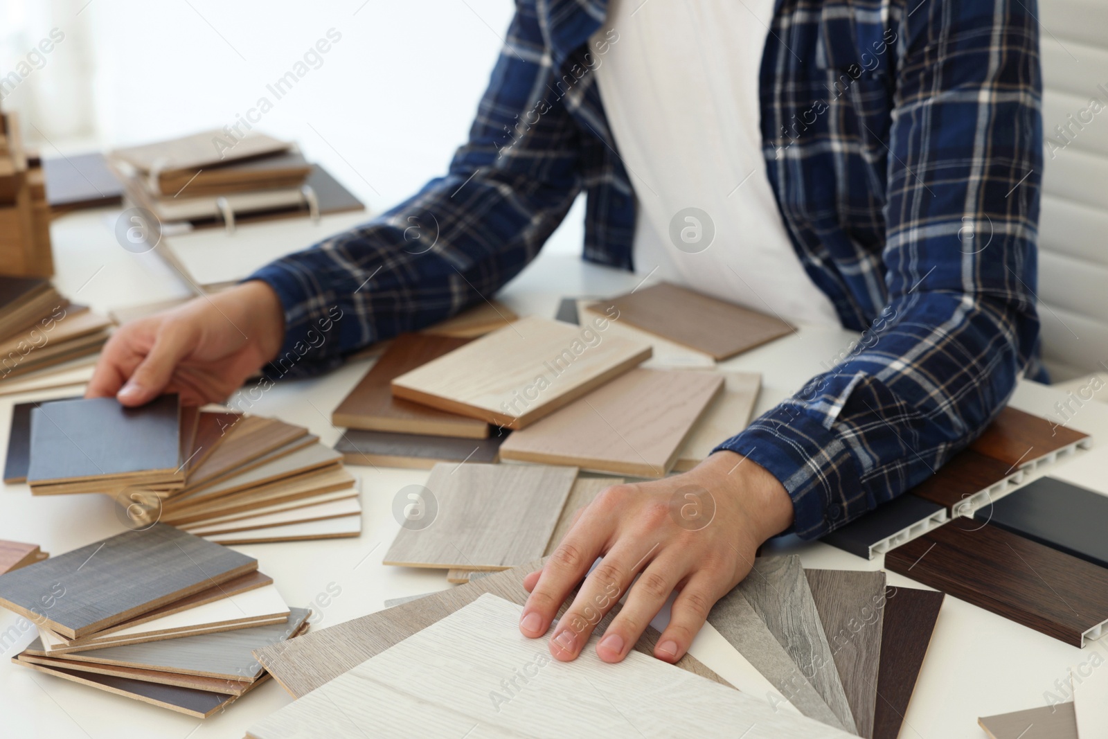 Photo of Man choosing wooden flooring among different samples at table, closeup