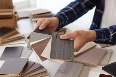 Photo of Man choosing wooden flooring among different samples at table, closeup