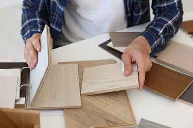 Photo of Man choosing wooden flooring among different samples at table, closeup