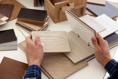 Photo of Man choosing wooden flooring among different samples at table, closeup