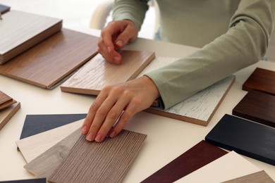 Photo of Woman choosing wooden flooring among different samples at table, closeup