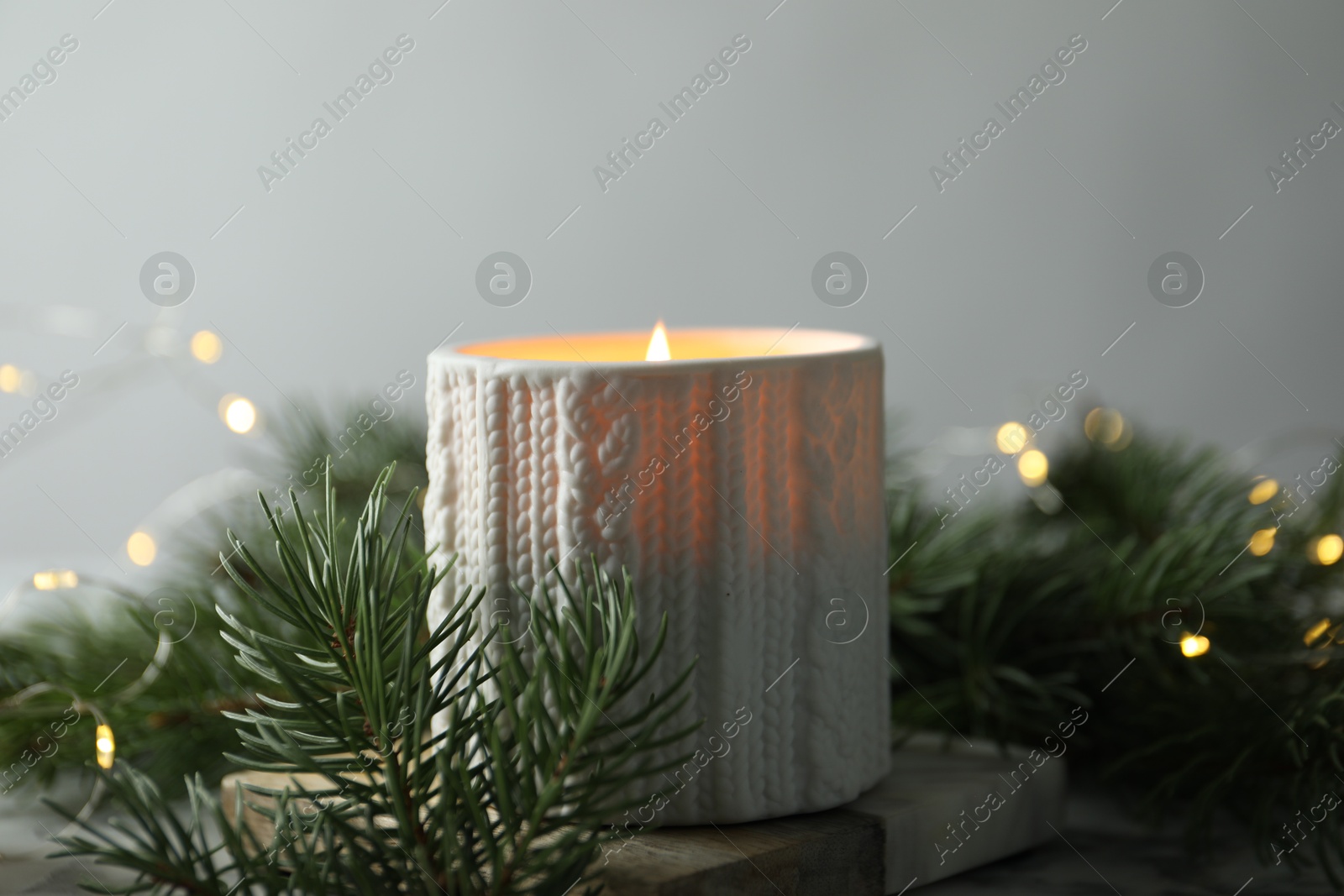 Photo of Burning candle, fir tree branches on table against blurred lights, closeup