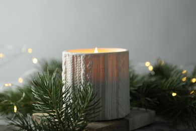 Photo of Burning candle, fir tree branches on table against blurred lights, closeup