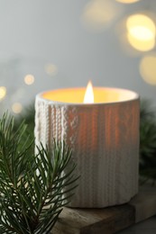 Photo of Burning candle, fir tree branches on table against blurred lights, closeup