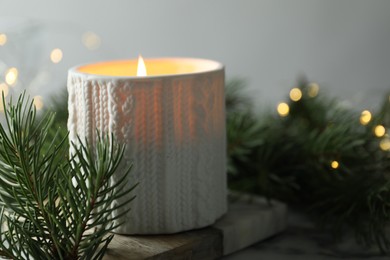 Photo of Burning candle, fir tree branches on table against blurred lights, closeup