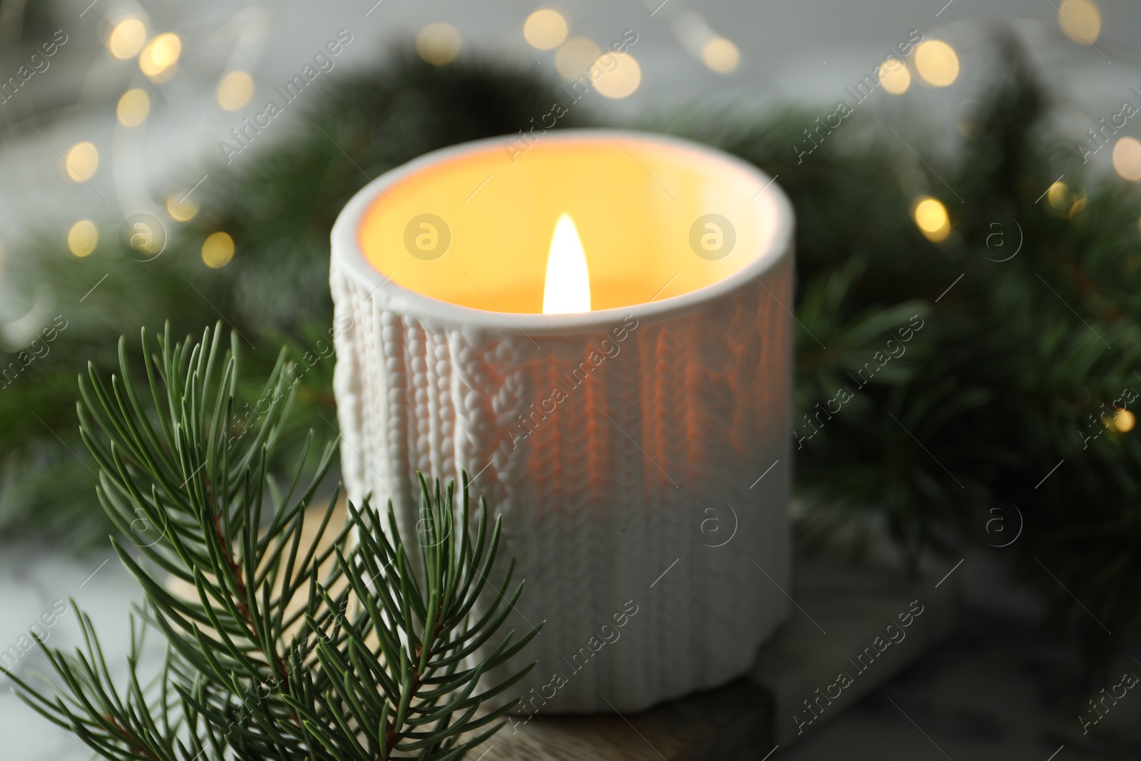 Photo of Burning candle, fir tree branches on table against blurred lights, closeup