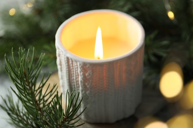 Photo of Burning candle, fir tree branches on table against blurred lights, closeup