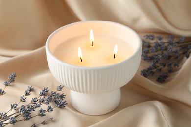 Burning candle and flowers on beige fabric, closeup