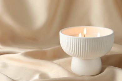 Burning candle on beige fabric, closeup. Space for text