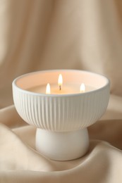 Stylish burning candle on beige fabric, closeup