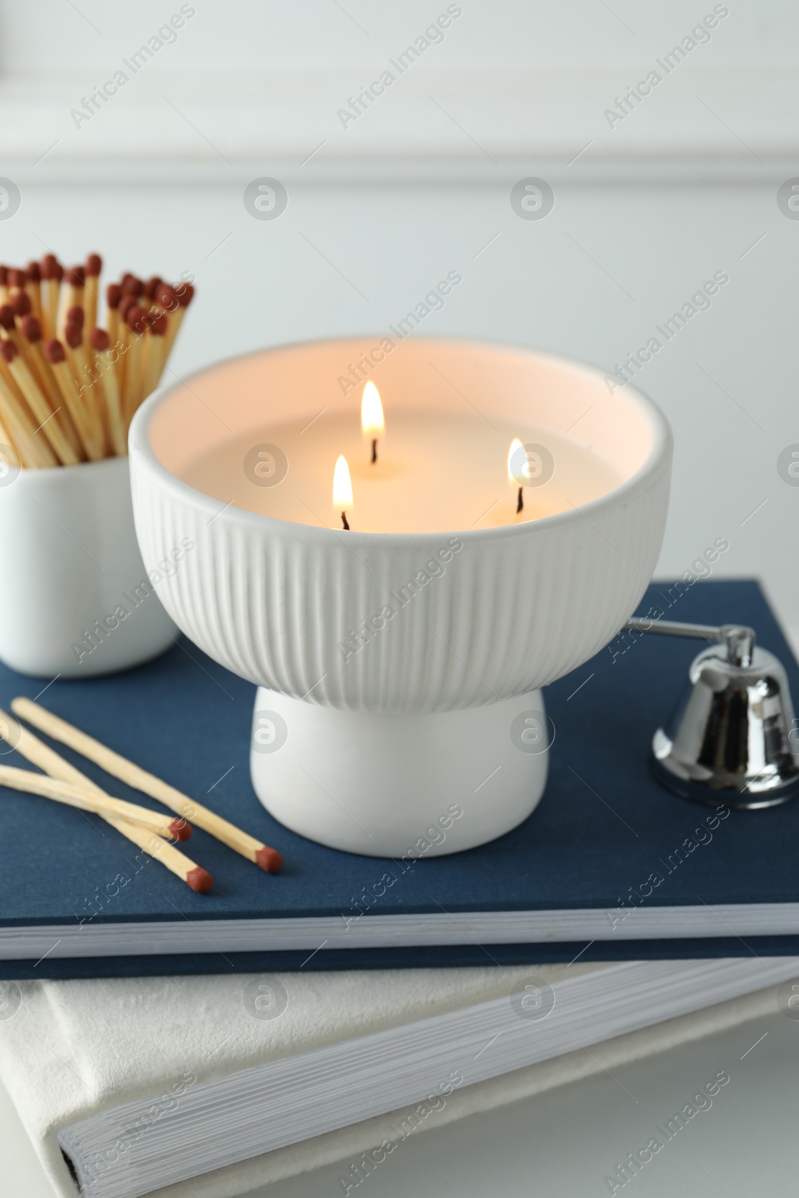 Photo of Burning candle, matches, books and bell on white marble table, closeup