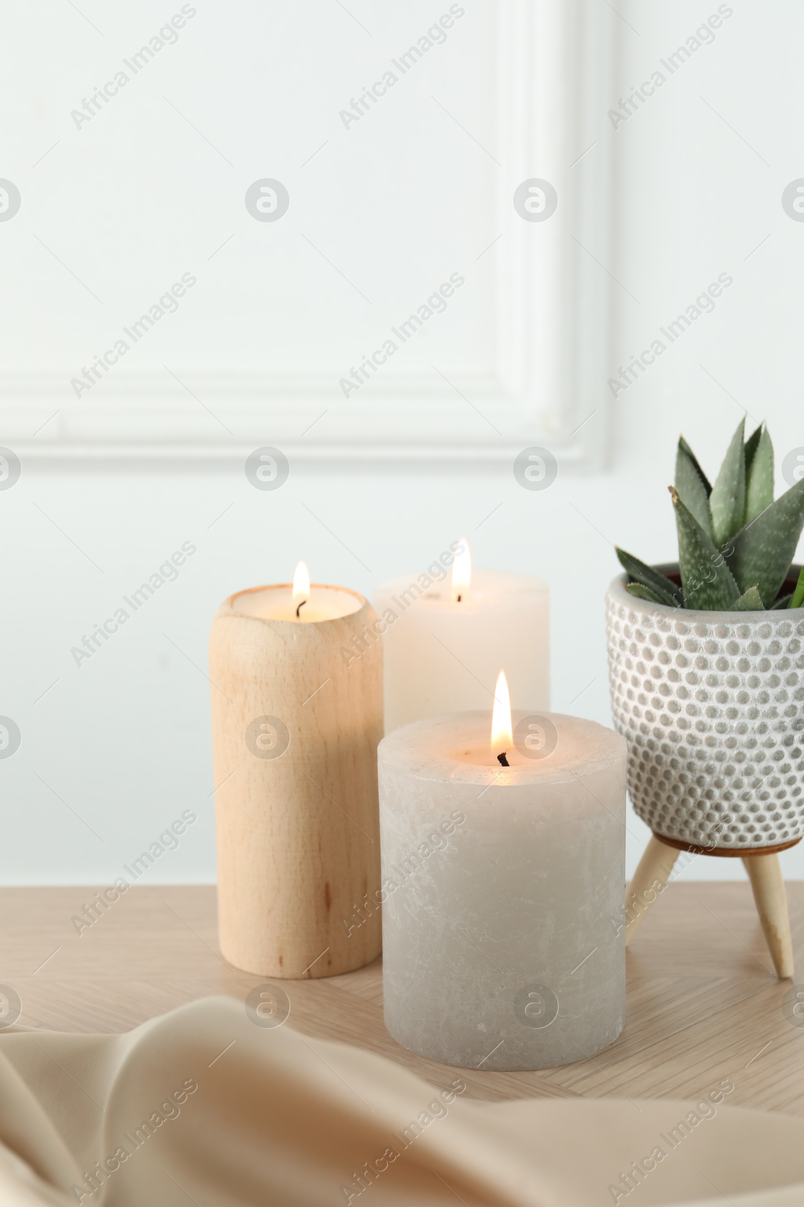 Photo of Beautiful burning candles, houseplant and cloth on wooden table, closeup