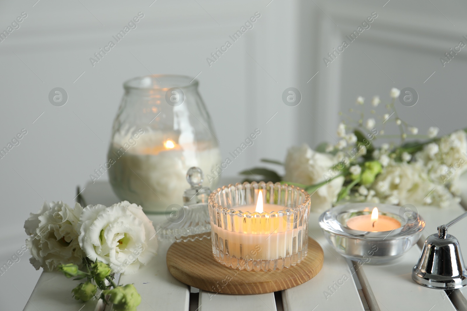 Photo of Beautiful burning candle and flowers on white wooden table